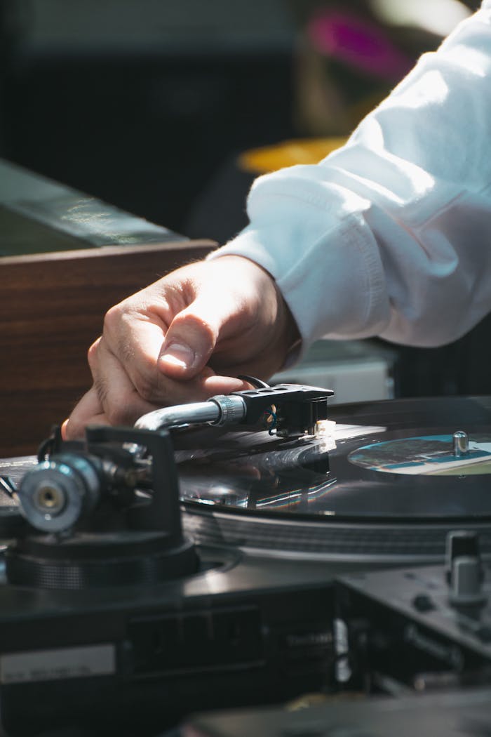 Man adjusting a vinyl record on a turntable indoors, capturing a retro music vibe.